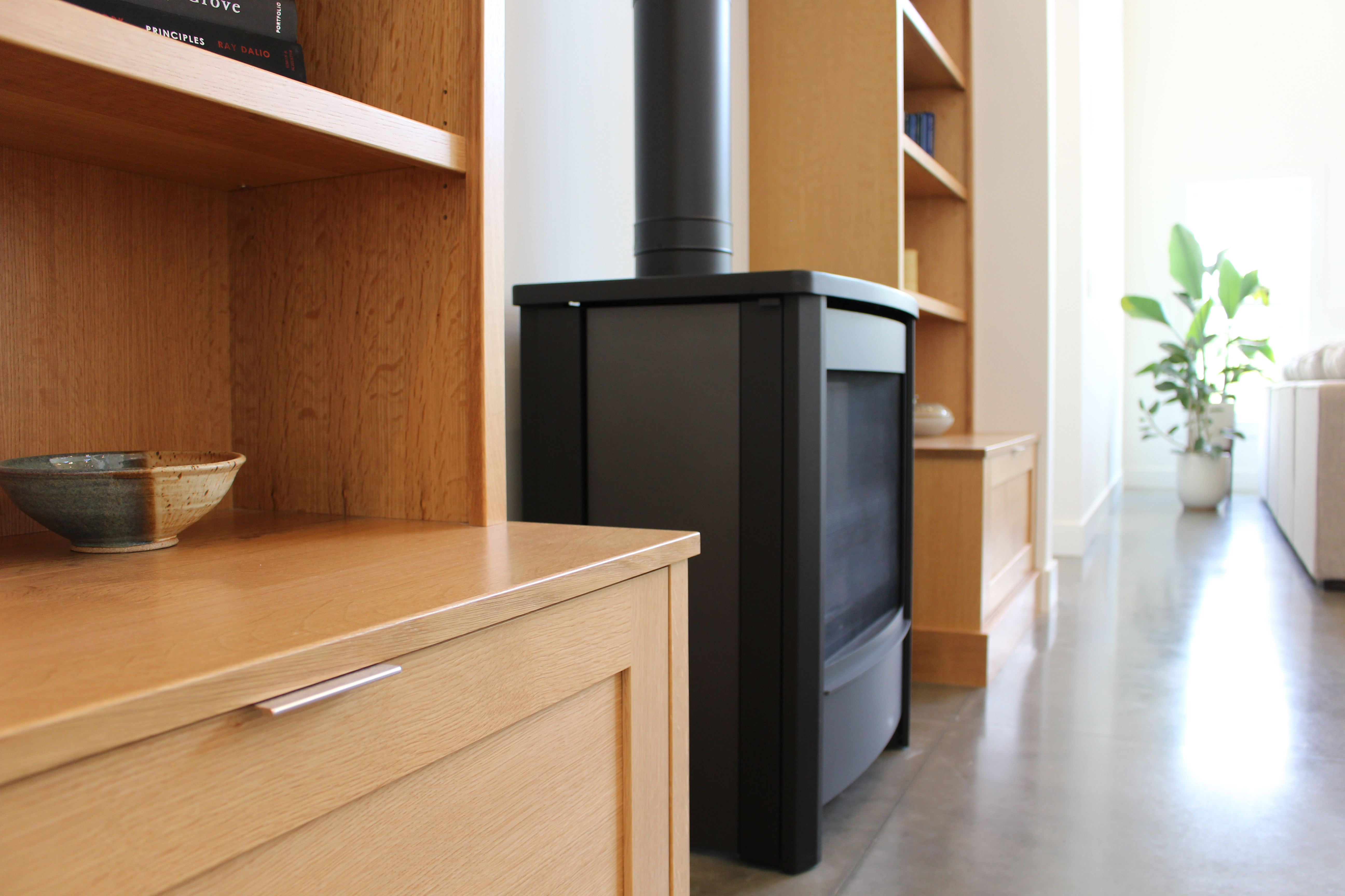 Close up of natural wood builtin cabinets with a black iron, wood burning stove on a polished concrete floor
