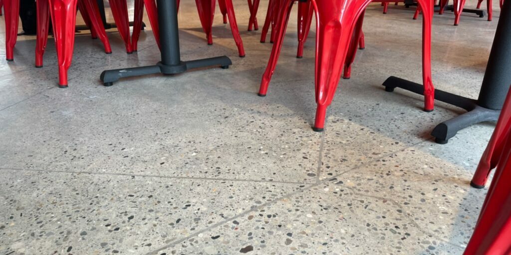 A polished concrete floor with a mix of small and large stones with saturated red dining chairs